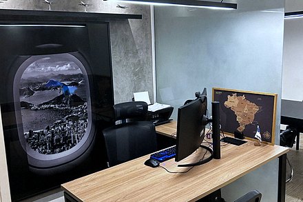 Estação de trabalho do escritório, com o painel da janela de avião ao fundo e um mapa do Brasil em cortiça sobre a mesa.